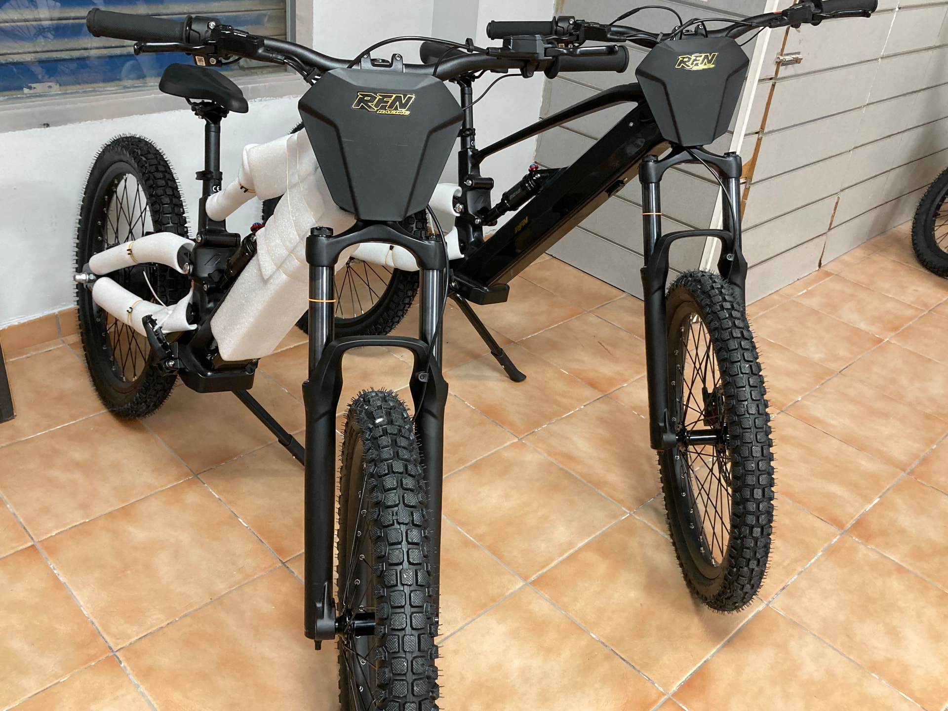 Dos bicicletas eléctricas de montaña RFN Racing en negro mate con el logotipo dorado en la tienda