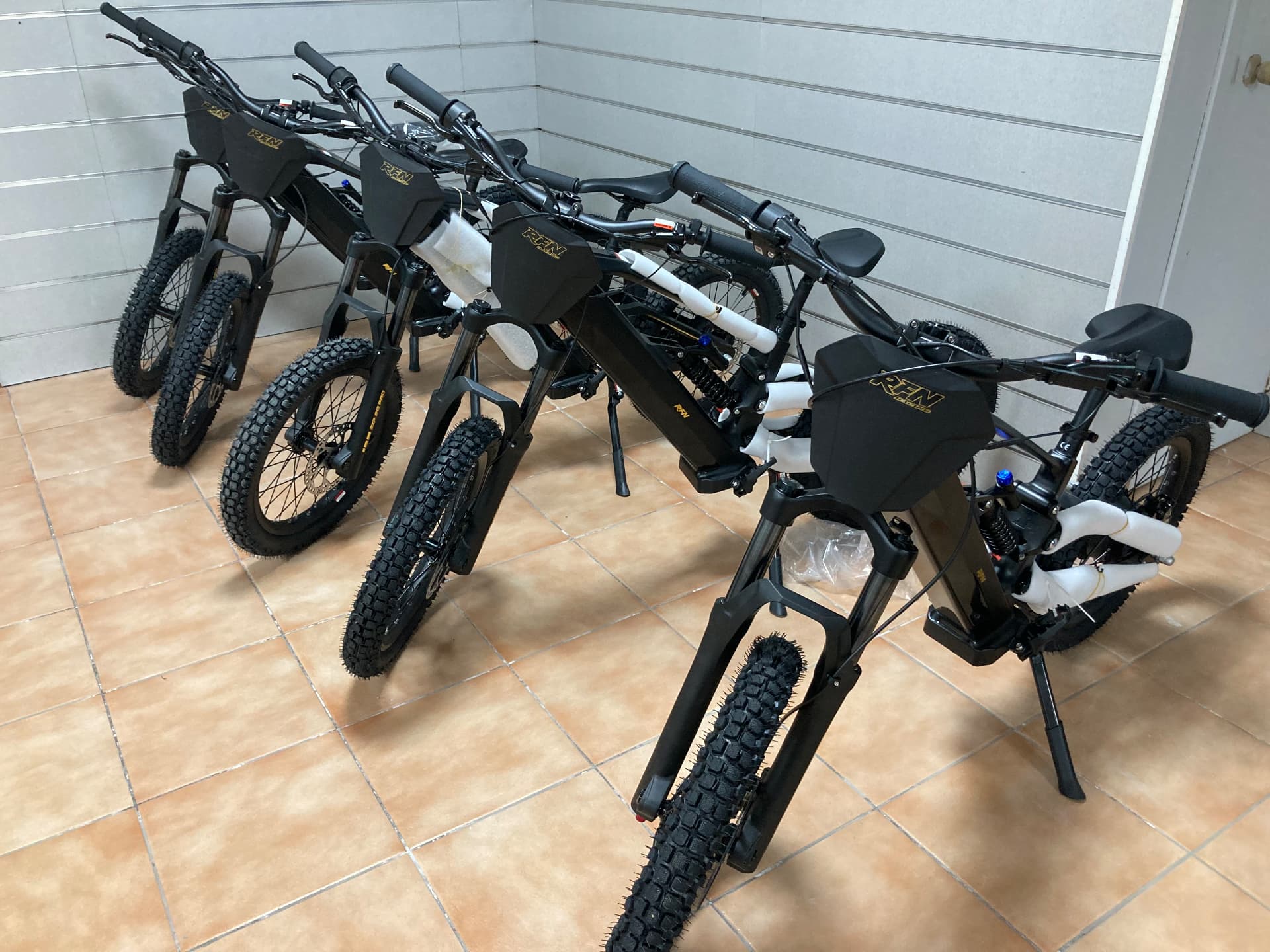 Fila de bicicletas eléctricas de montaña RFN Racing en negro con placas portanúmeros doradas en la exposición