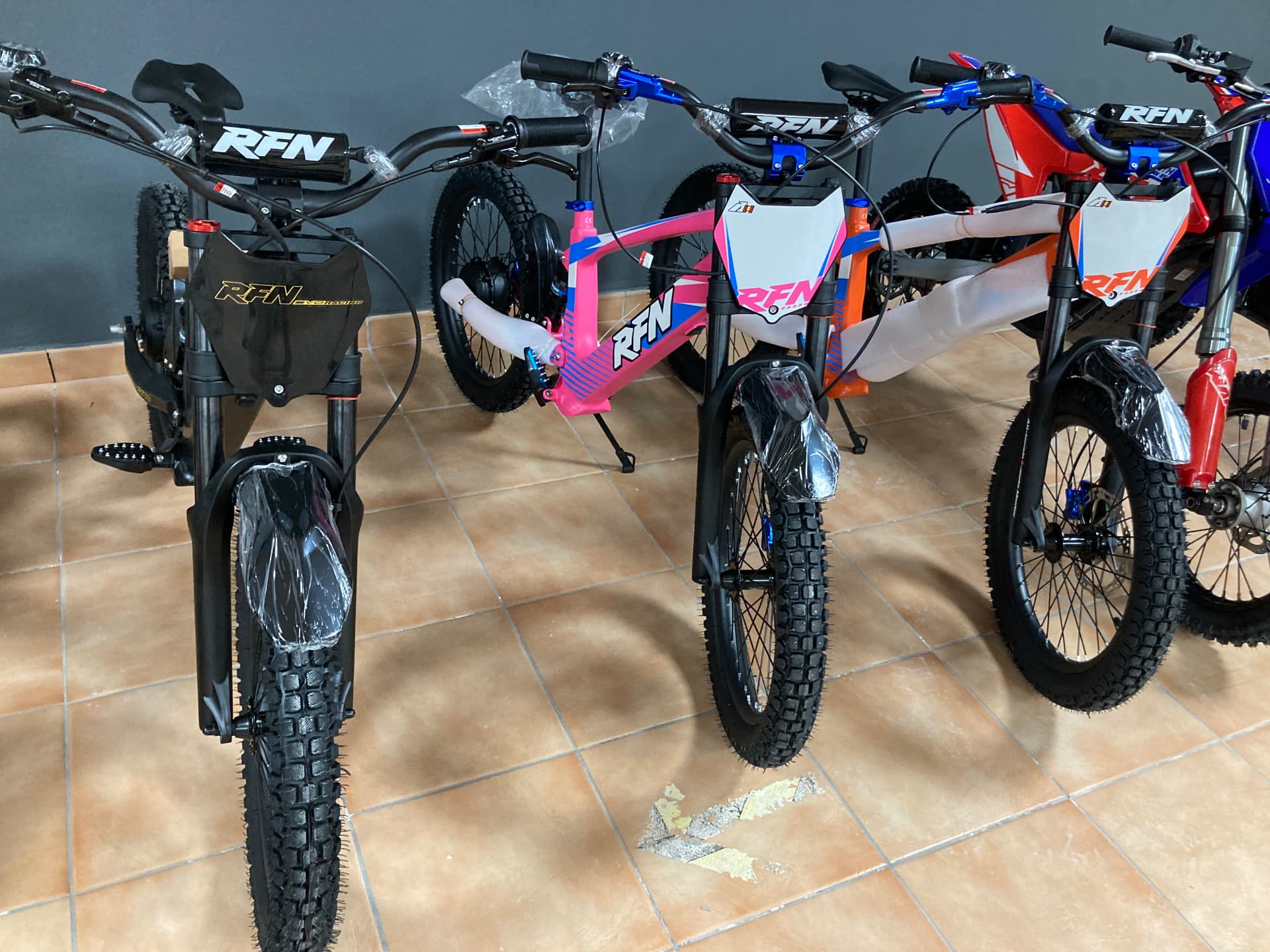 Bicicletas eléctricas todoterreno RFN estilo motocross en negro, rosa y naranja alineadas en la tienda