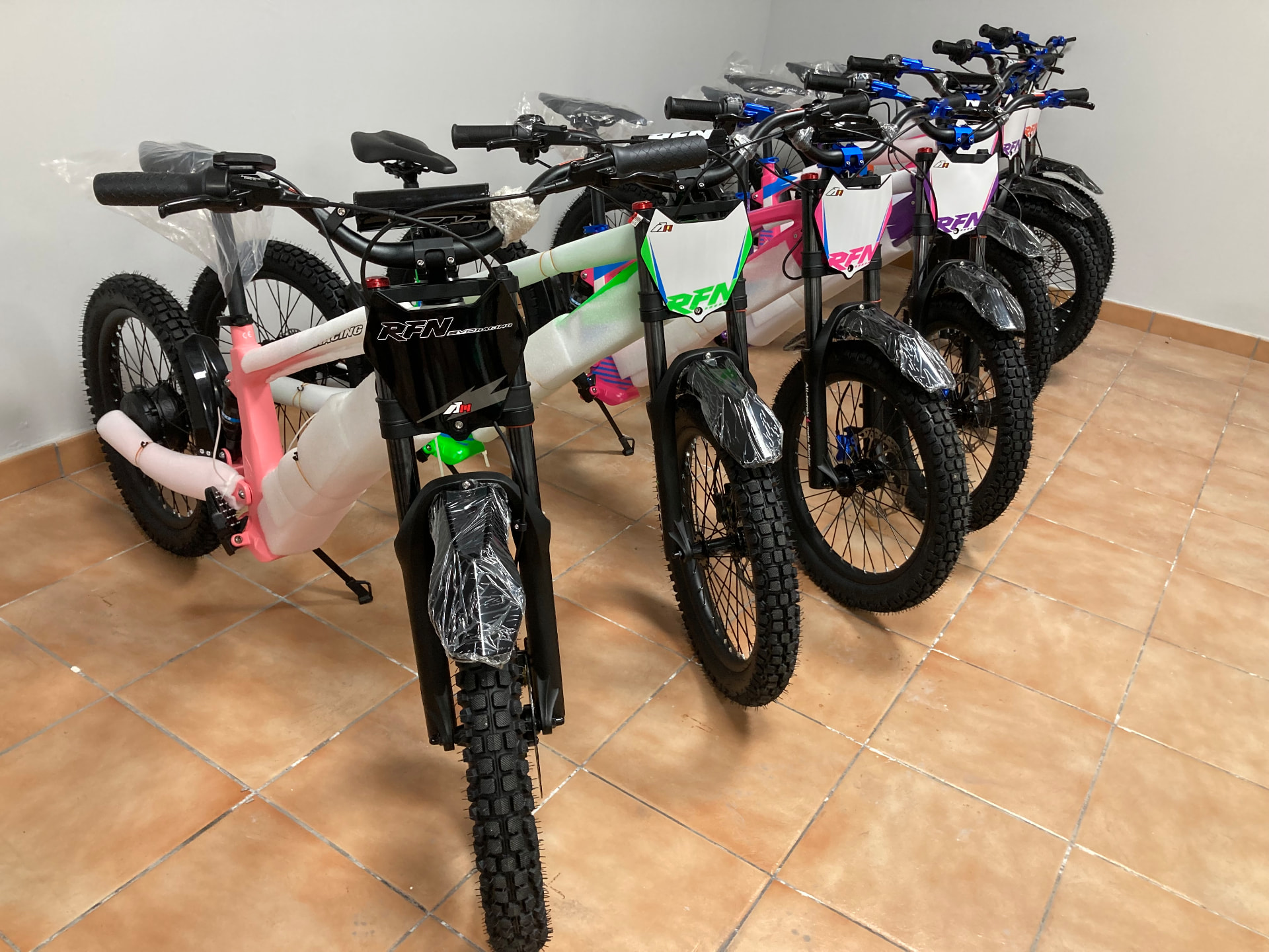 Fila de bicicletas eléctricas infantiles RFN EVO Racing en blanco, rosa y verde con la placa 41 en primer plano