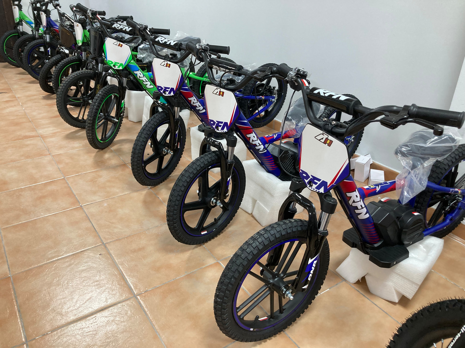 Bicicletas eléctricas infantiles RFN de aprendizaje todoterreno en azul marino con franjas rojas y blancas, y en verde, alineadas en la tienda