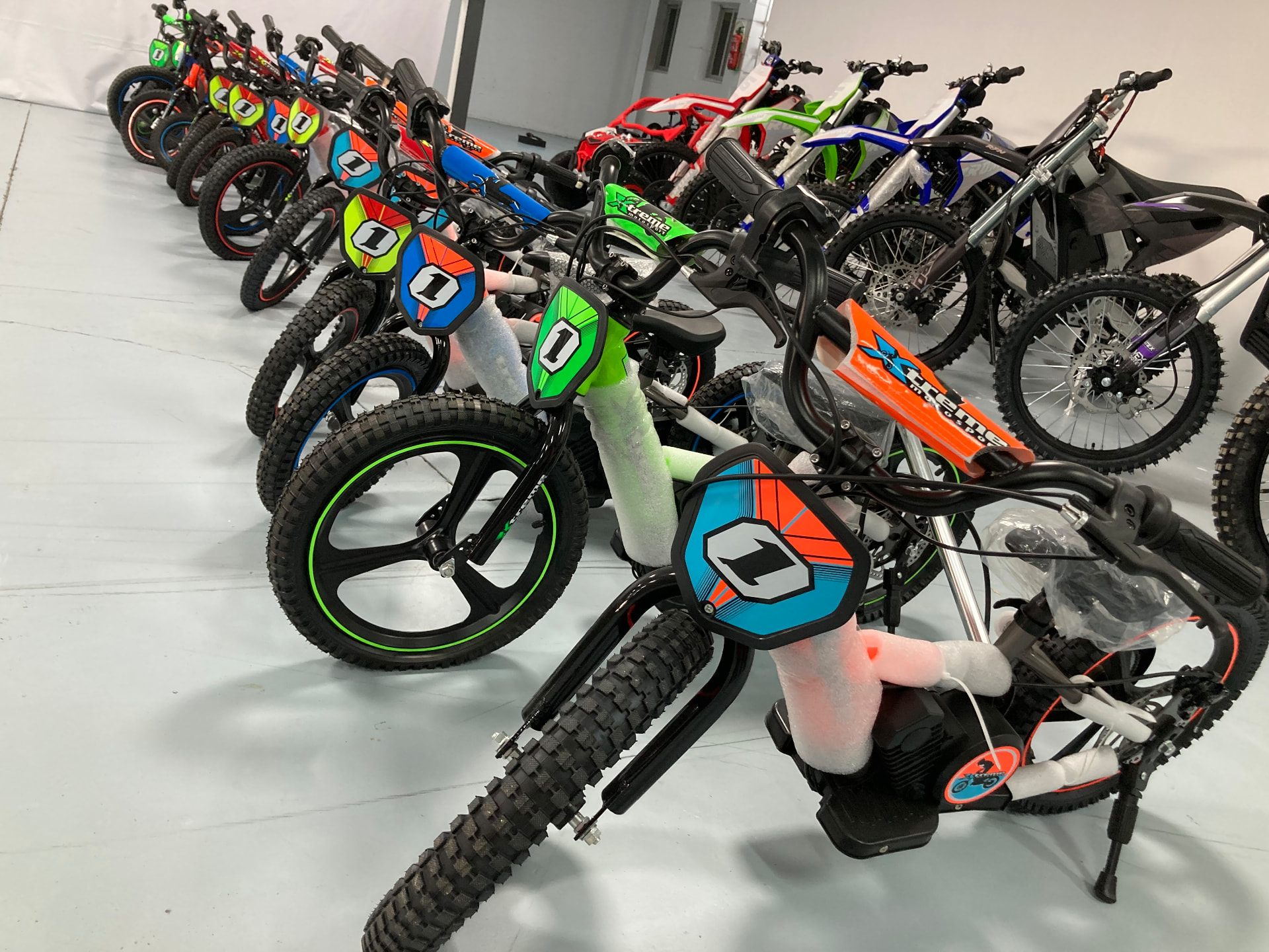Bicicletas eléctricas infantiles Xtreme con el dorsal 1 en negro con detalles naranja, turquesa y verde lima en el almacén