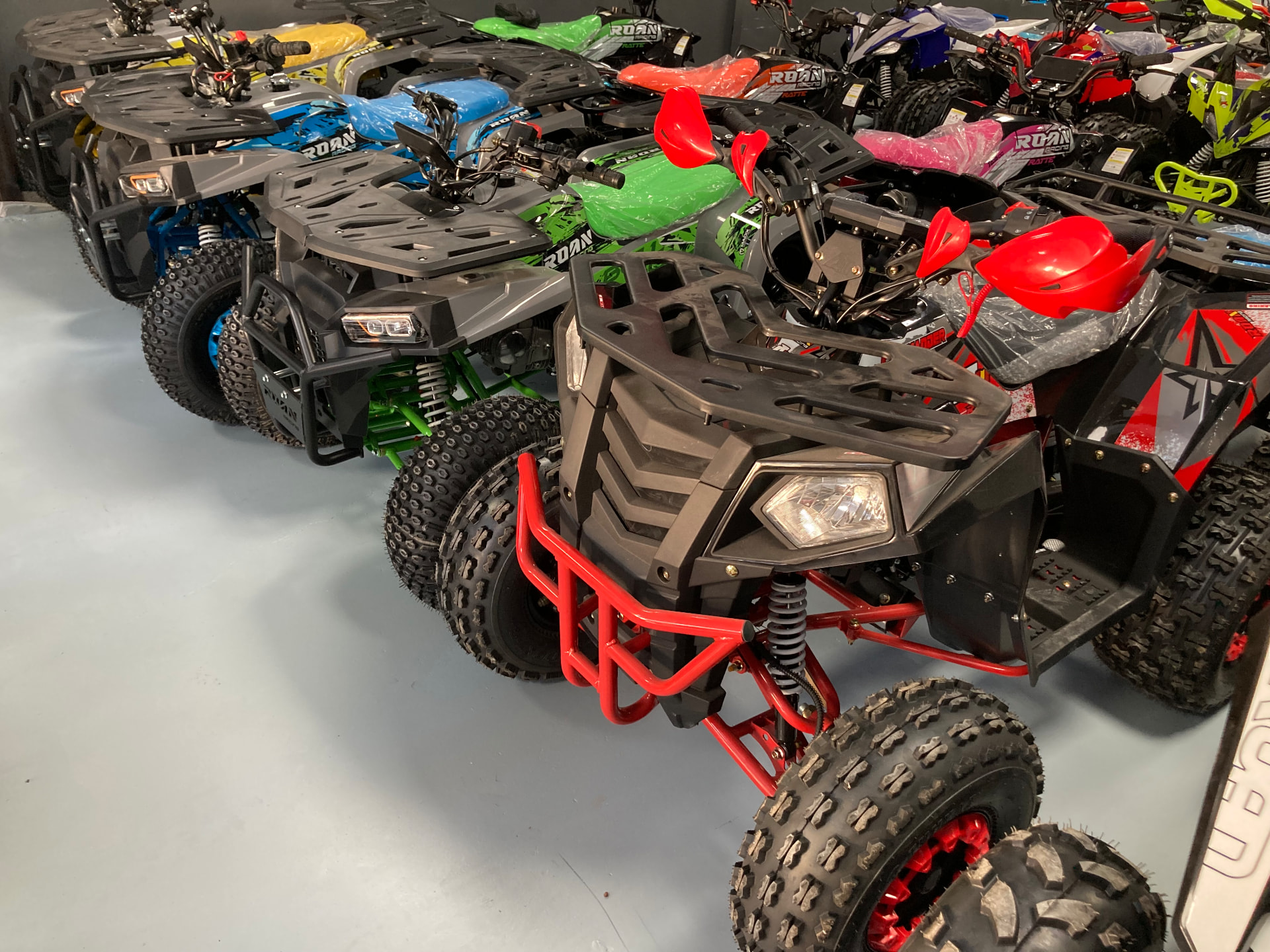 Quads utilitarios ROAN con parrilla frontal en negro, gris y azul alineados en la tienda